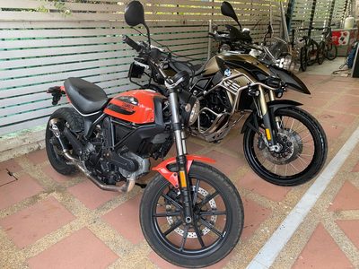 A Ducati Scrambler and a BMW parked under a carport.