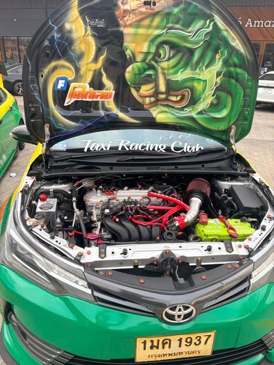 A green and yellow Bangkok taxi with its bonnet raised.