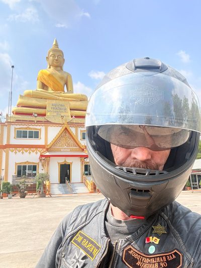 A motorcyclist in a helmet in front of a large gold Buddha.